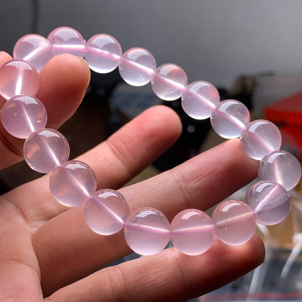 A hand - held natural rose quartz bead bracelet, showcasing smooth, round beads with a soft, translucent pink hue.