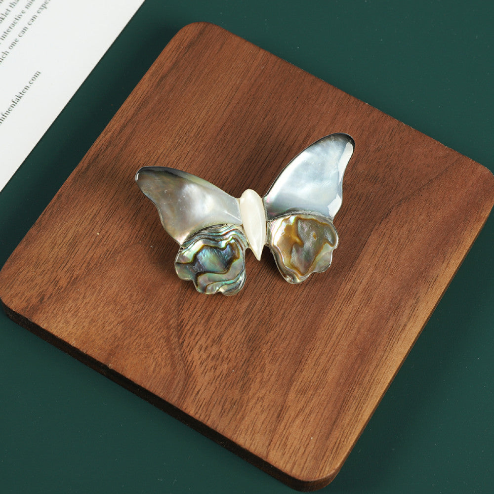 This elegant butterfly brooch is handcrafted from natural mother-of-pearl and iridescent abalone shell, showcasing unique organic patterns. A perfect nature-inspired accessory to elevate any outfit