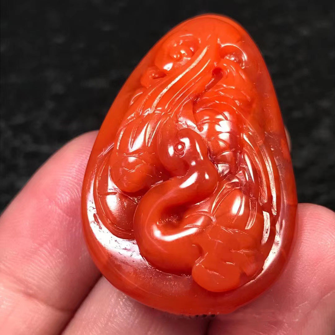 A hand held natural south red agate pendant, exquisitely carved into the shape of a phoenix, showcasing vivid red color and fine craftsmanship.