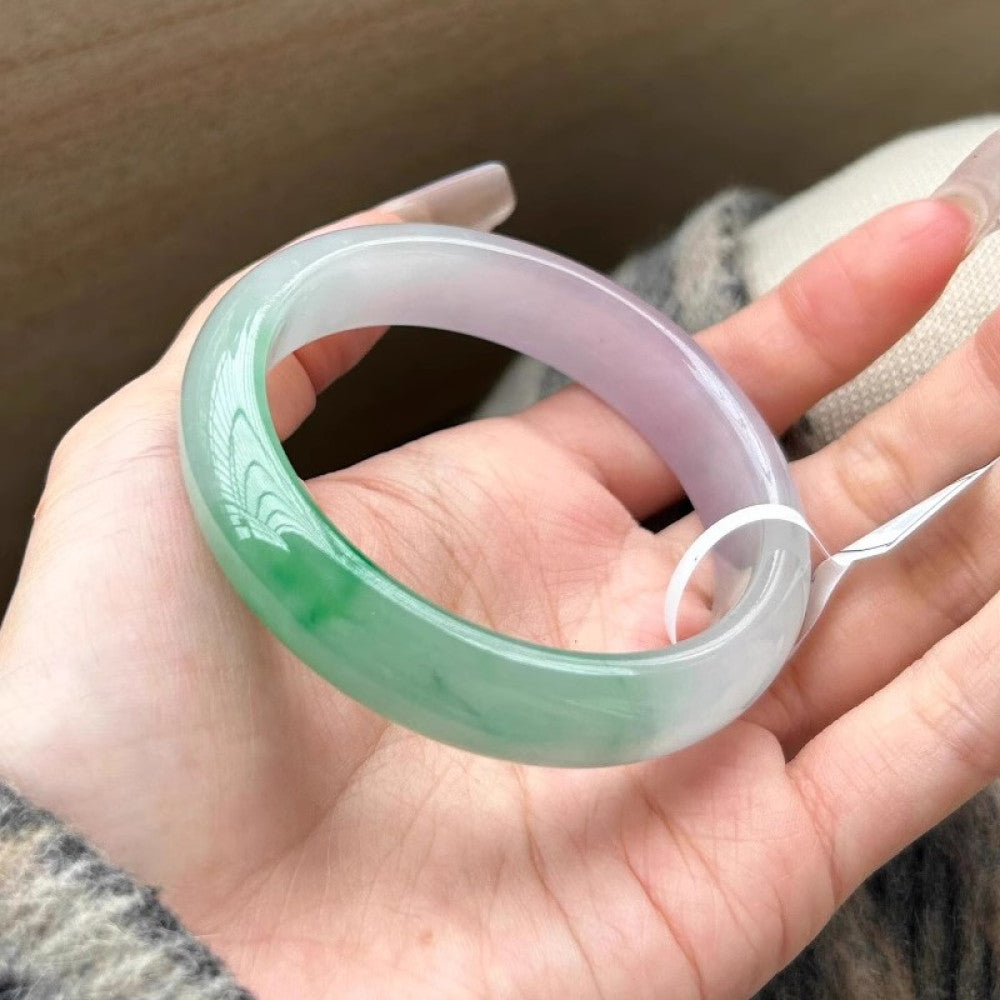 Hand holding natural spring color jadeite bangle with green and lavender hues, featuring a white tag