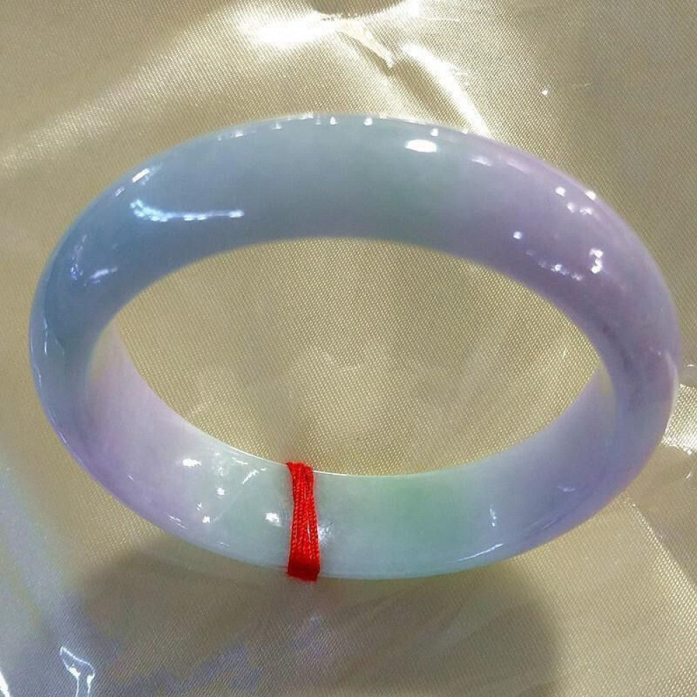 Natural spring color jadeite bangle featuring lavender and green hues, tied with red string on glossy fabric background