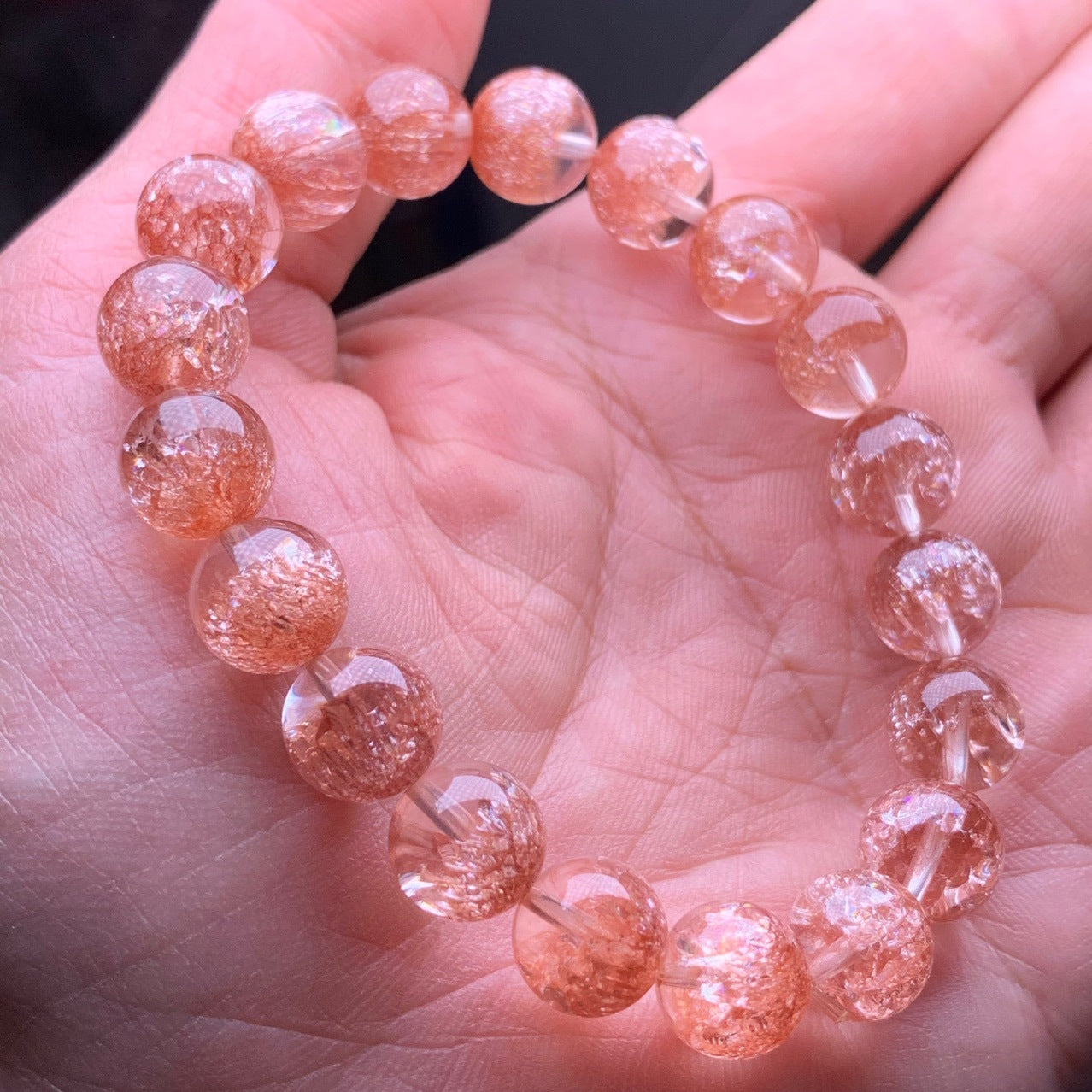 A hand - held natural strawberry quartz bead bracelet, featuring round beads with a soft pinkish - orange hue and visible internal inclusions that give it a sparkling appearance.