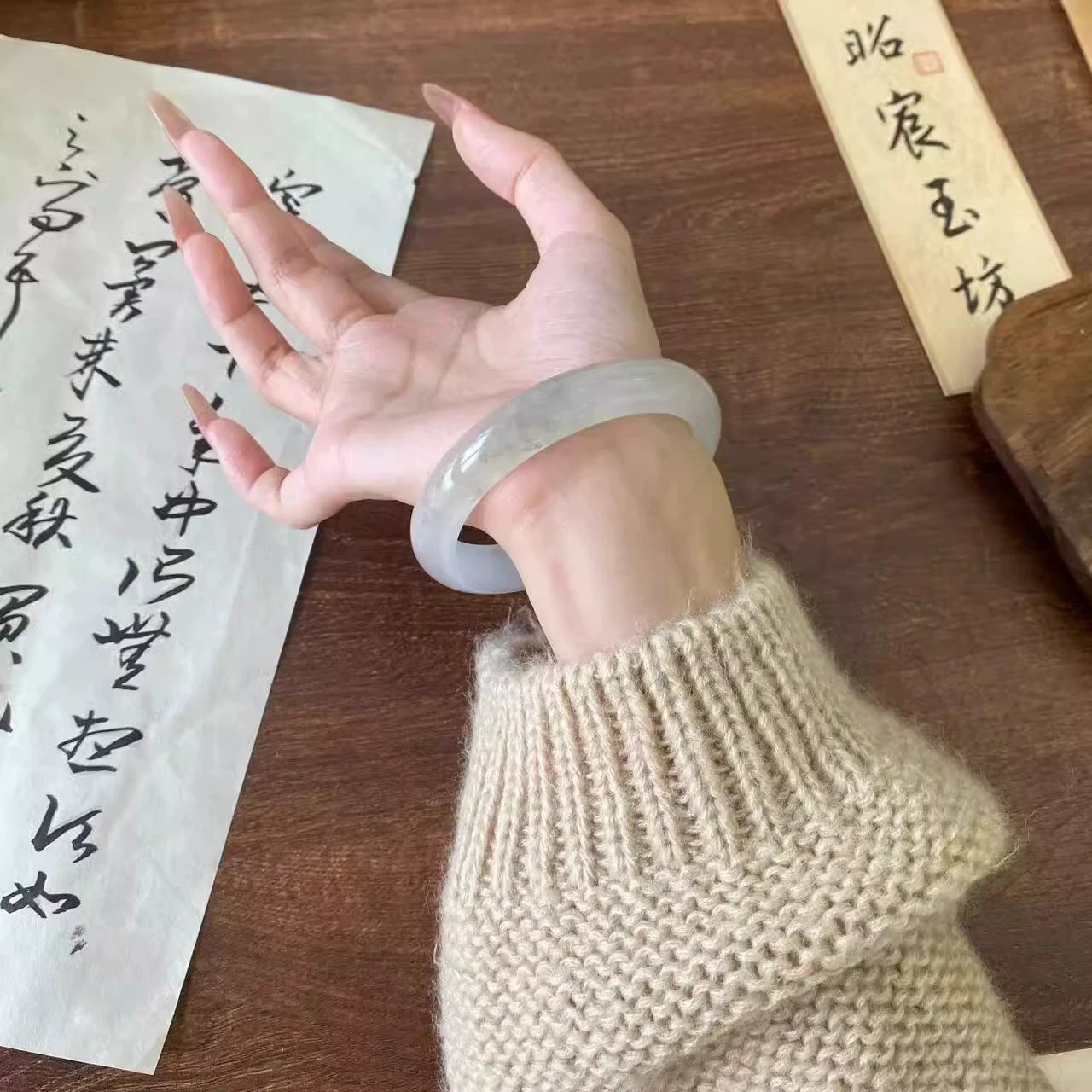 Hand wearing natural translucent icy jade bangle with Chinese calligraphy background