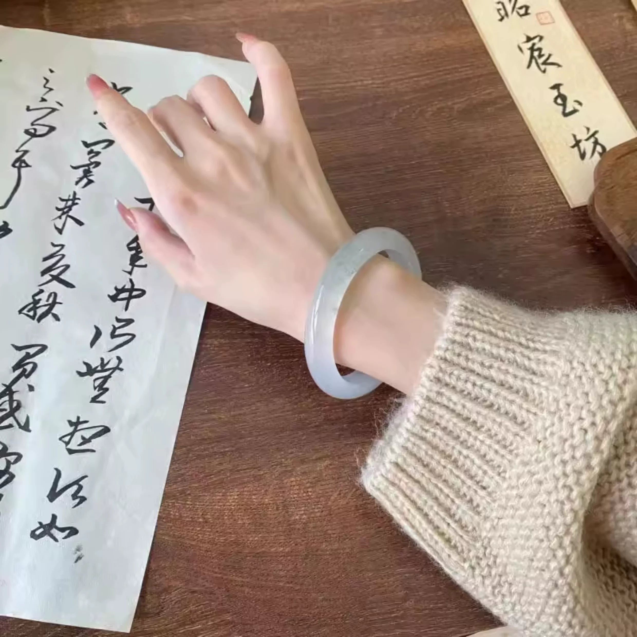 Hand wearing natural translucent icy jade bangle with Chinese calligraphy background 01