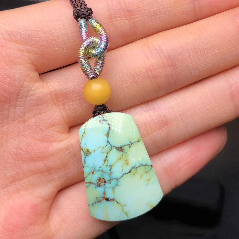 A hand - held necklace featuring a natural turquoise pendant with distinct matrix patterns, a beeswax bead, and a colorful knotted cord.