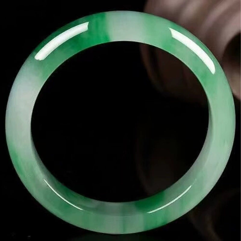 Natural vivid green gradient jadeite bangle against black background with glossy finish