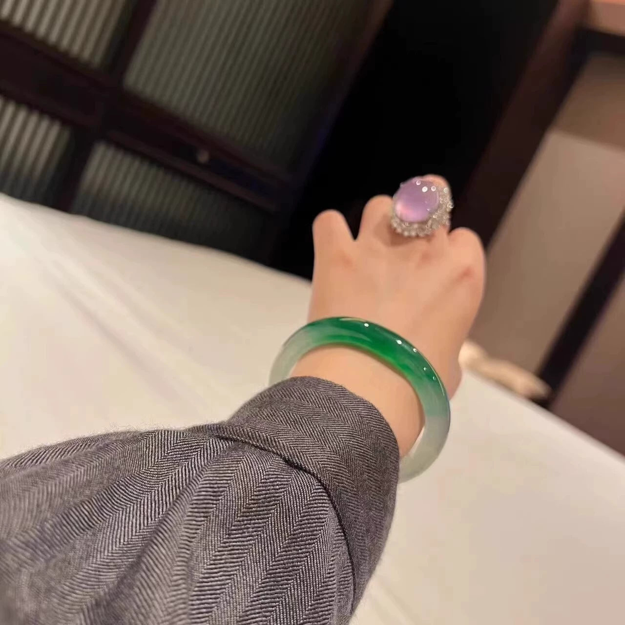 Hand wearing natural vivid green gradient jadeite bangle and lavender gem ring in elegant setting