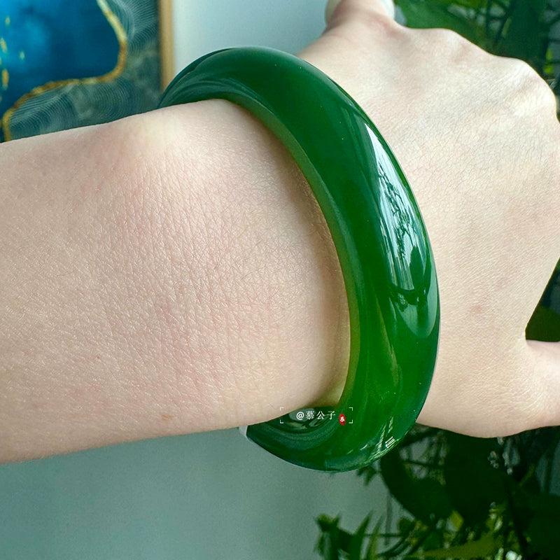 Hand wearing natural vivid green jade bangle against green plants background 01