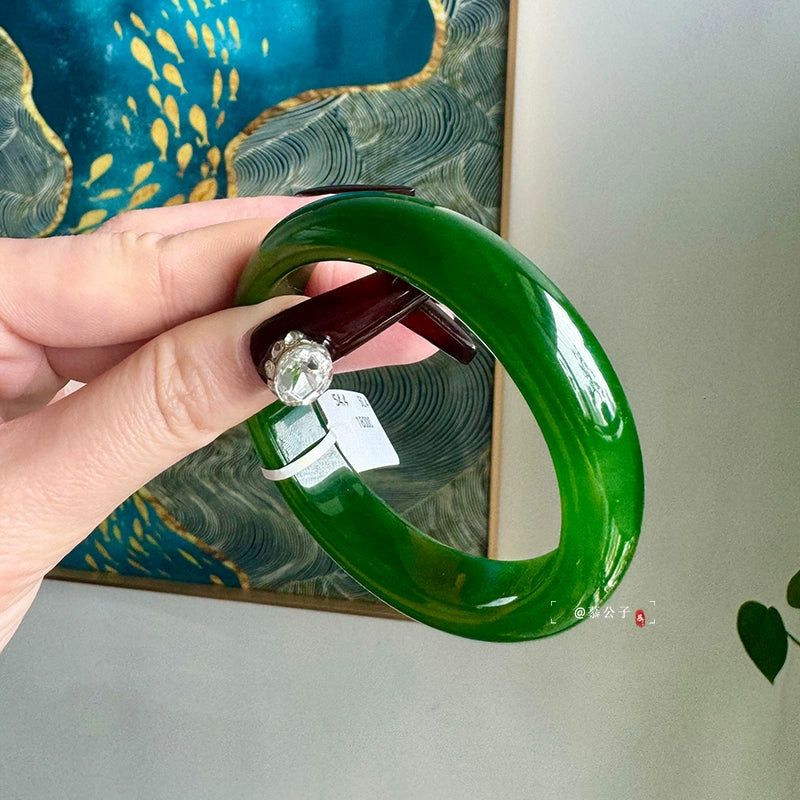 Hand wearing natural vivid green jade bangle against green plants background
