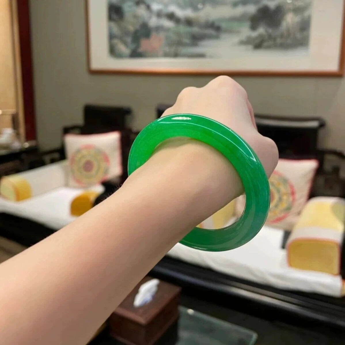 Hand wearing natural vivid green jadeite bangle in Chinese style interior with painting and traditional furniture