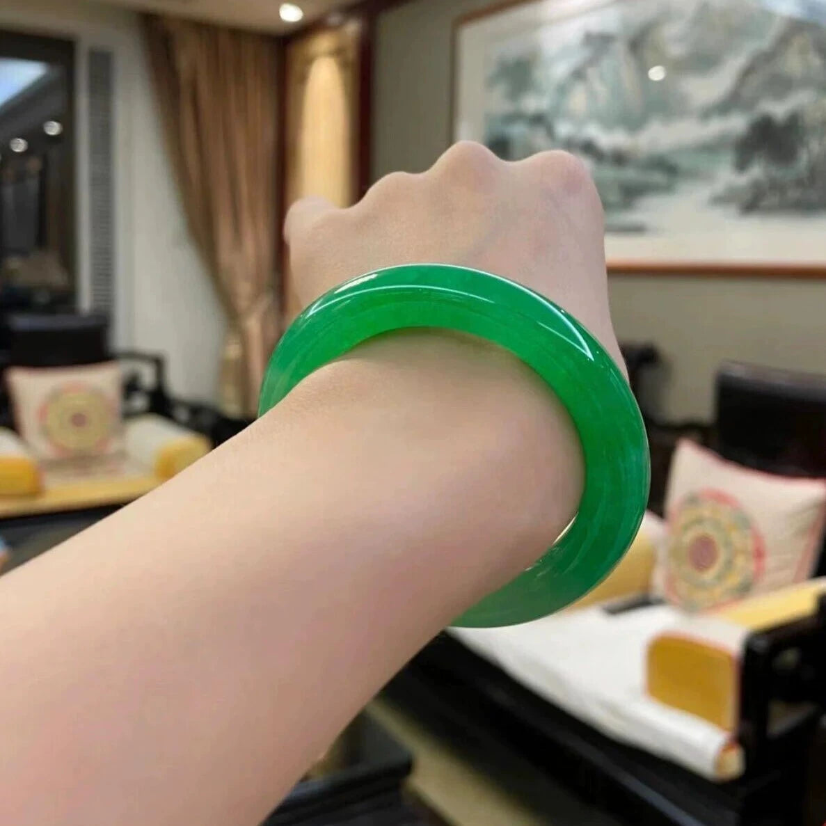 Hand wearing natural vivid green jadeite bangle in Chinese style interior with painting and traditional furniture 01