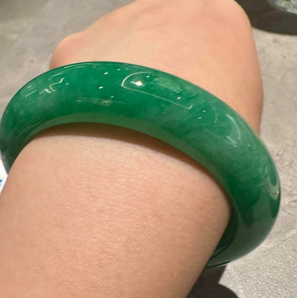 Hand wearing natural vivid green jadeite bangle against neutral background