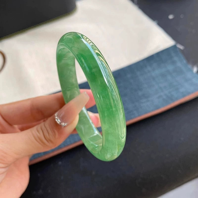 Hand holding natural vivid green jadeite bangle with fabric background