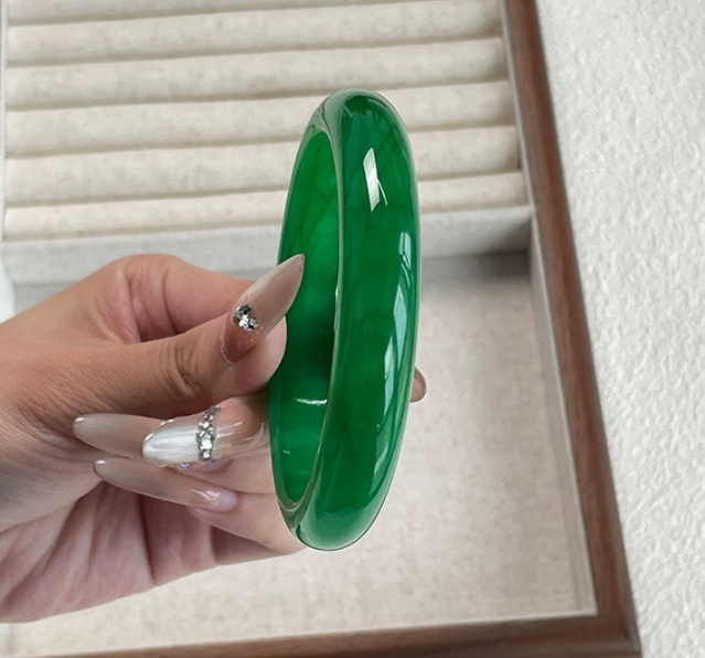 Hand holding natural vivid green jadeite bangle against jewelry display background