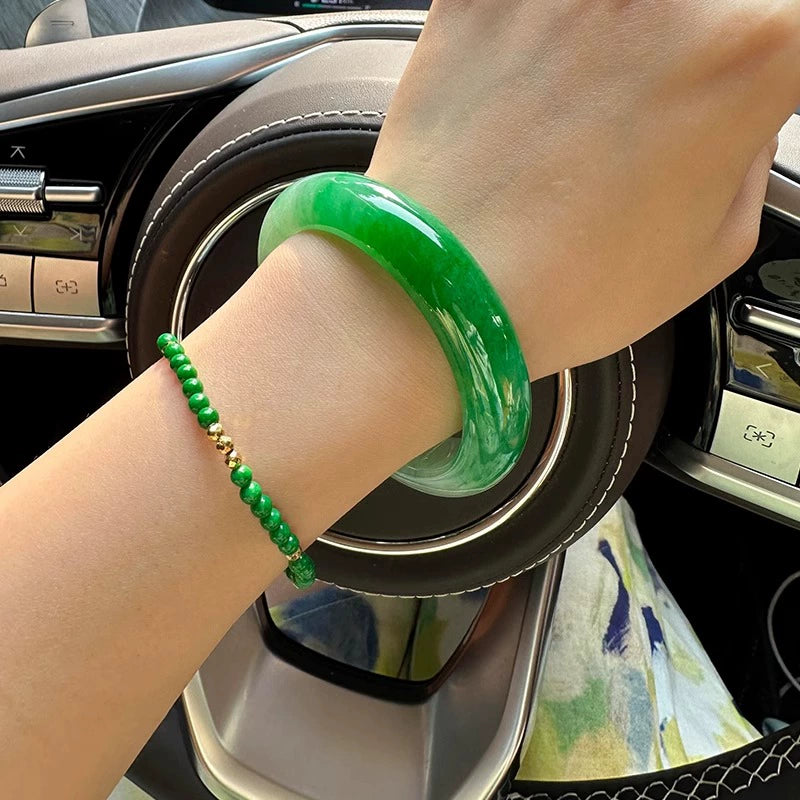 Hand wearing natural vivid green jadeite bangle and matching jade bracelet in car interior