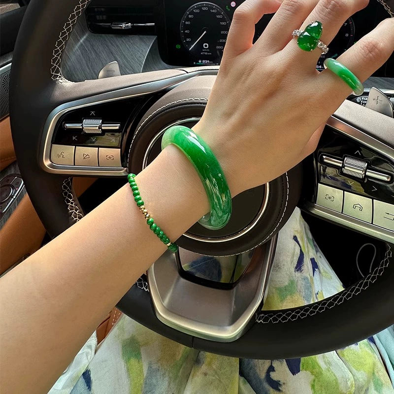 Hand wearing natural vivid green jadeite bangle and matching jade bracelet in car interior 01