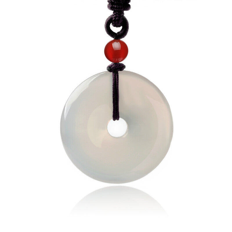 Natural white jade peace button pendant, featuring a smooth and round design, complemented by a red agate bead, strung on a dark cord.