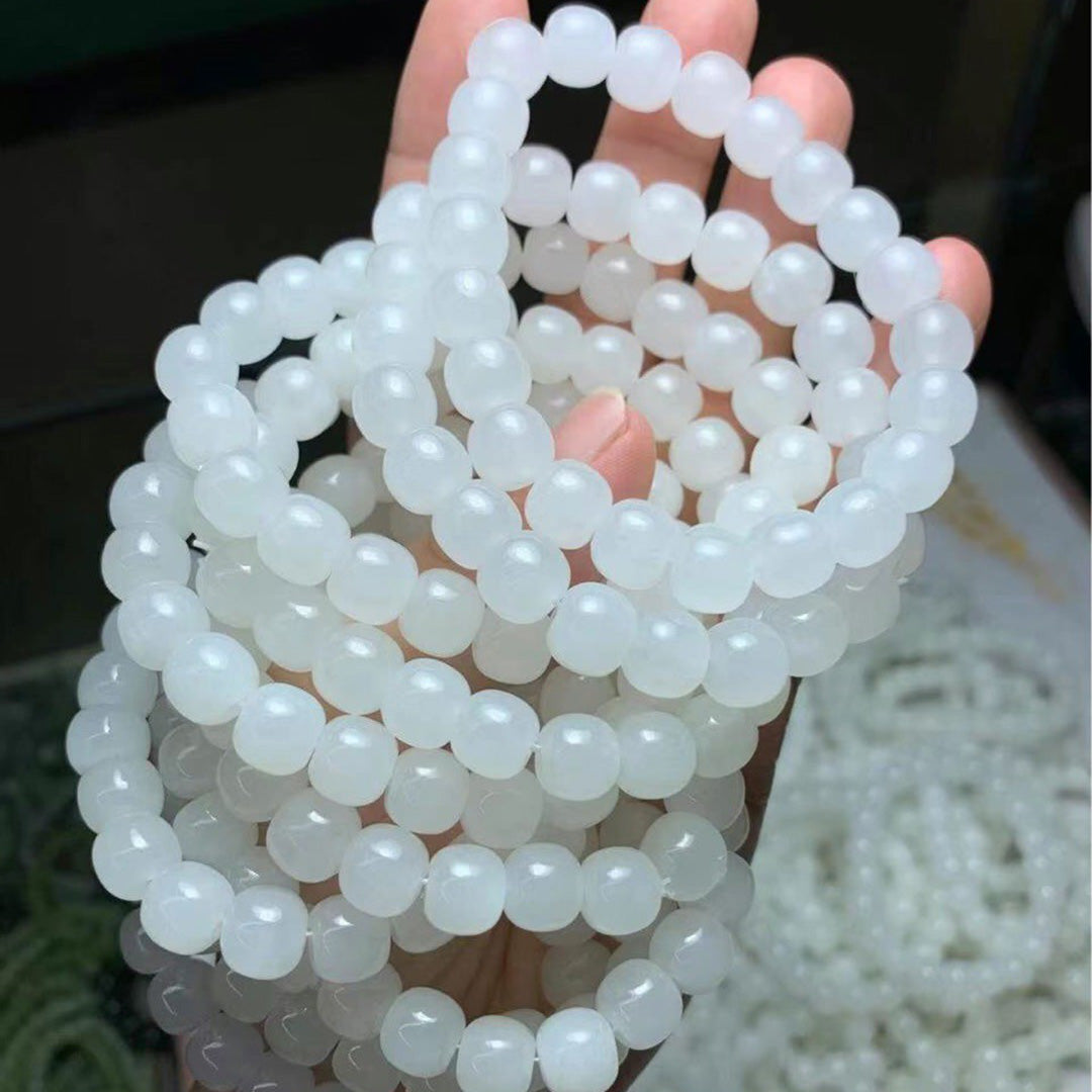 Set of natural white jadeite bead bracelets held in a hand, featuring smooth and round beads with a soft, milky - white hue.