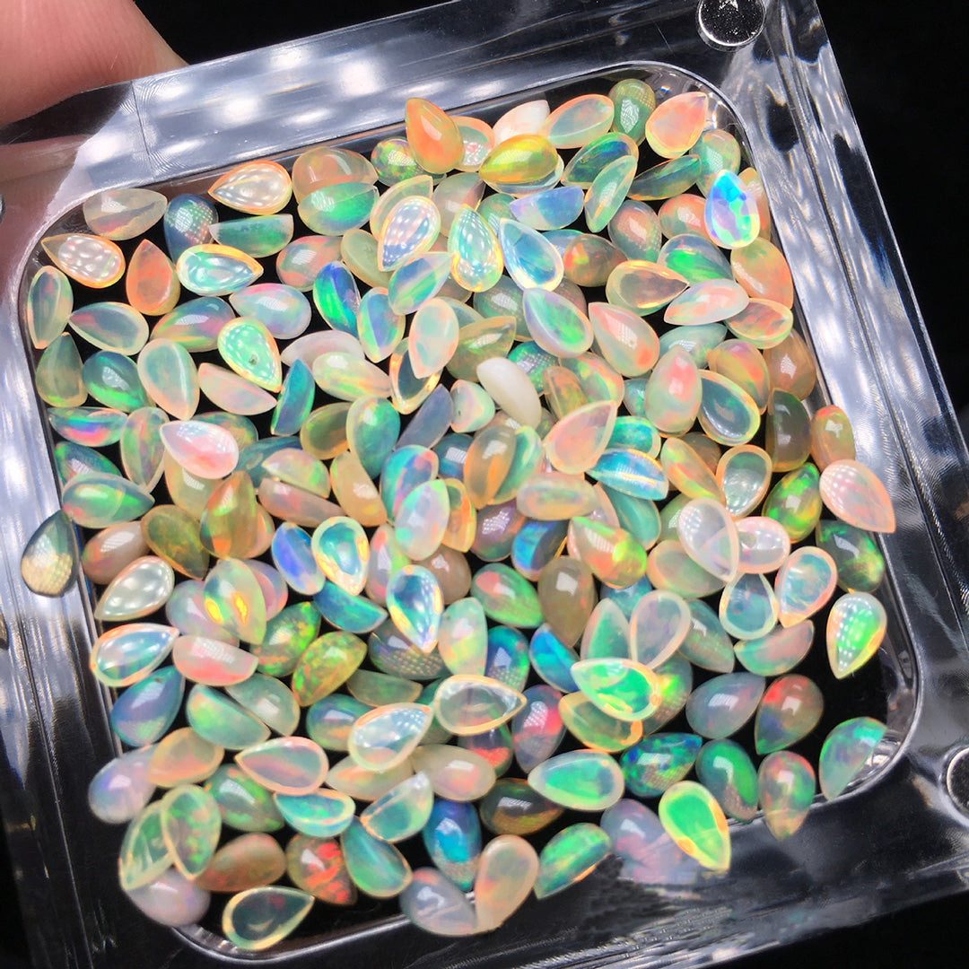 The teardrop-shaped opal loose stone in the transparent box is colorful and shows a color change effect.