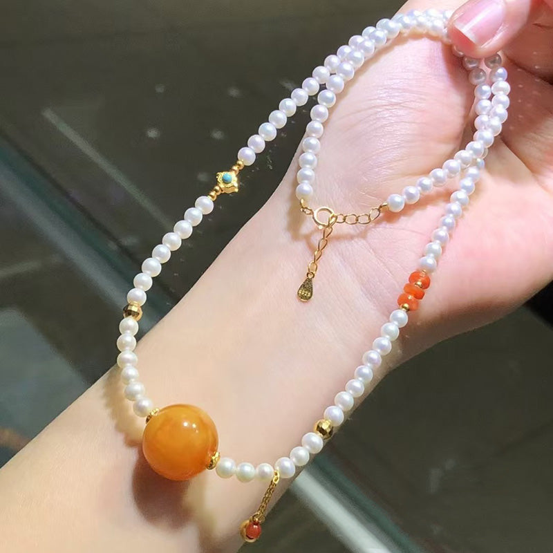 A beautiful necklace featuring white pearls, a large orange - hued amber bead, gold - toned metal accents, and small red beads, perfect for adding an elegant touch to any look