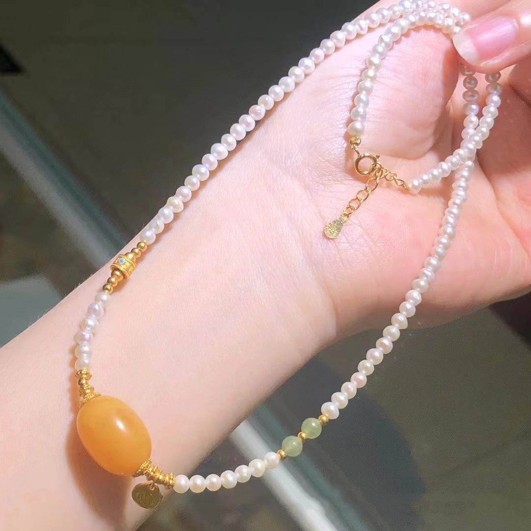 elegant white pearl necklace featuring a large oval amber pendant, green jade beads, and gold - plated metal components, suitable for both casual and formal occasions