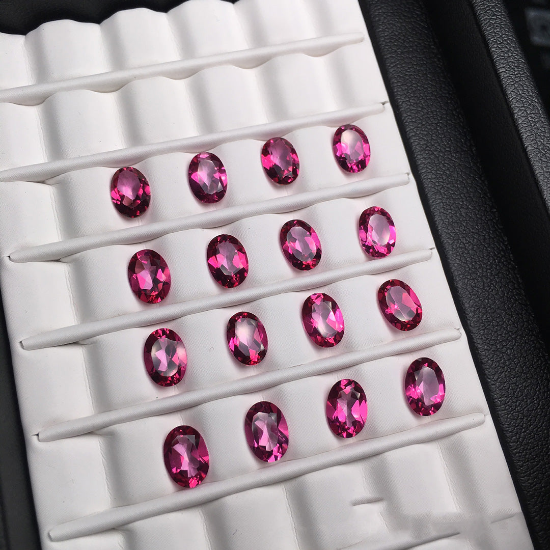 Several oval-cut rose-colored gemstone rough stones are neatly arranged on a white mount, with vivid colors.
