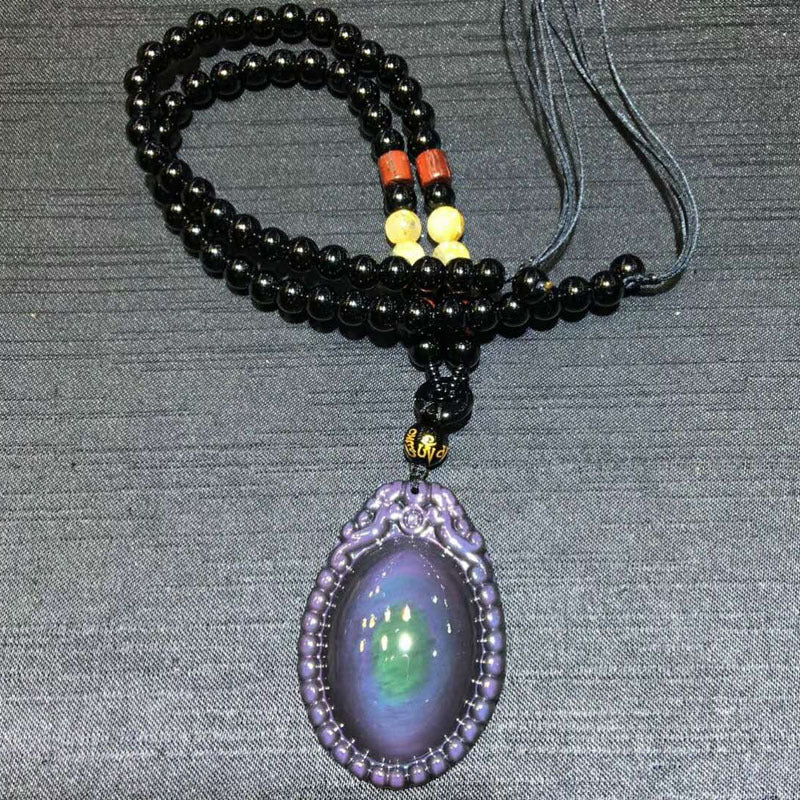 A necklace featuring a rainbow eye obsidian pendant, black obsidian beads, red agate beads, and beeswax beads, with a black cord.