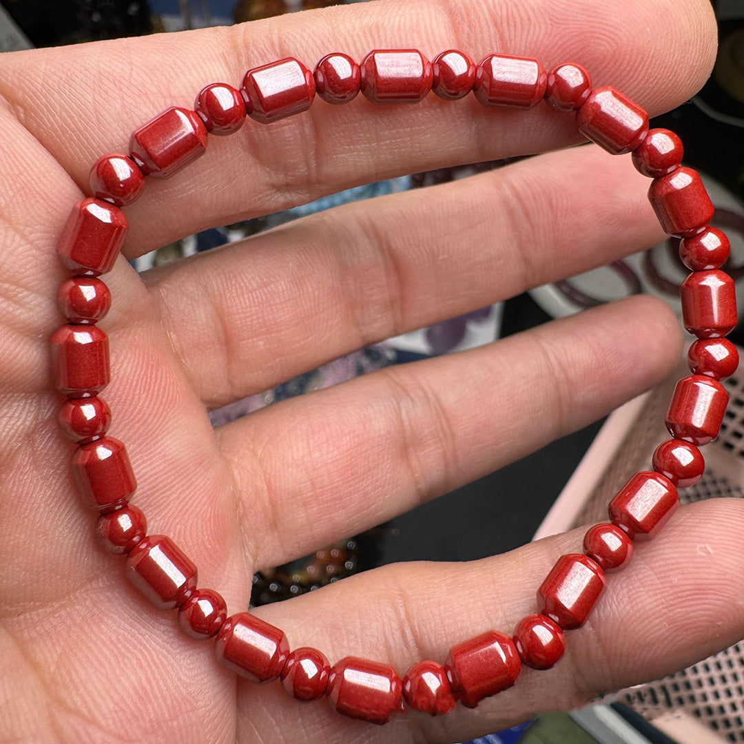 A hand - held red cinnabar bead bracelet featuring a mix of round and cylindrical beads, showcasing a vivid red color and glossy surface.