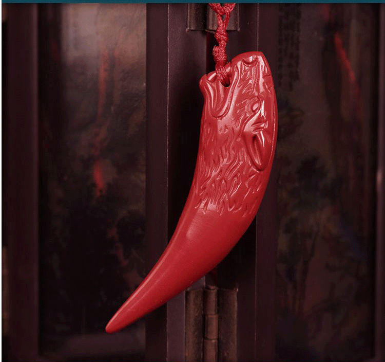 Red cinnabar pendant intricately carved into the shape of a wolf tooth, attached to a red rope, set against a dark - toned background.