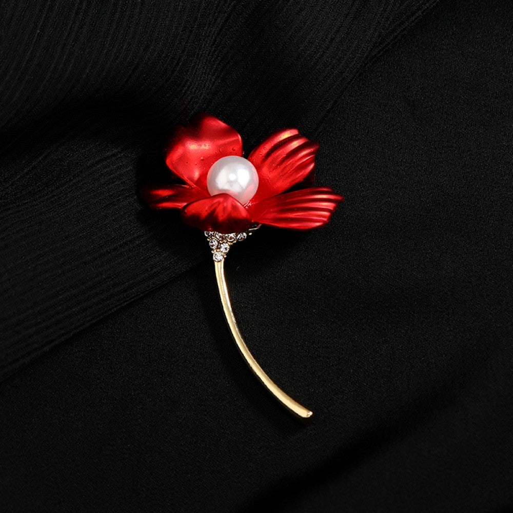 This elegant brooch features vibrant red petals with a lustrous pearl center, set on a gold stem with sparkling crystal accents. A romantic, eye-catching accessory