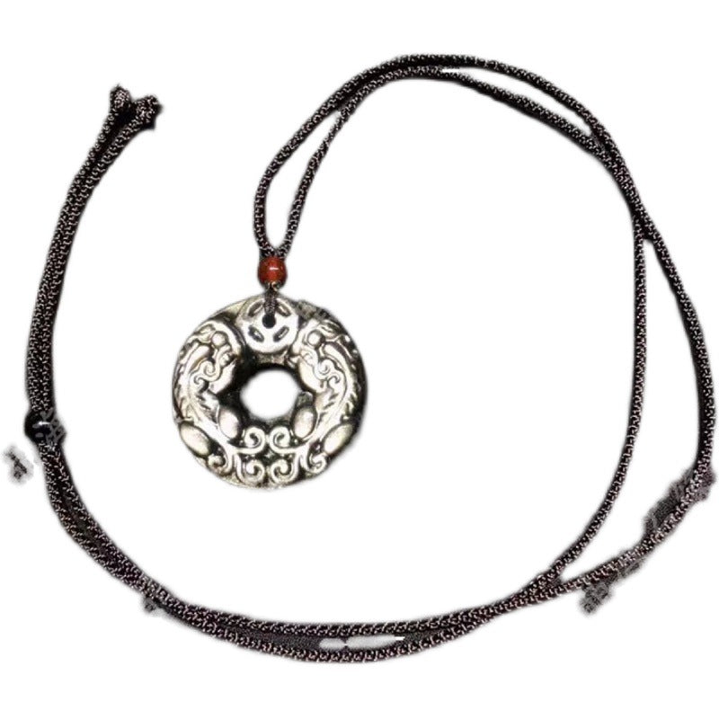 Sterling silver pendant featuring a peace button design with intricate double - dragon carvings, complemented by a red agate bead, attached to a braided cord necklace.