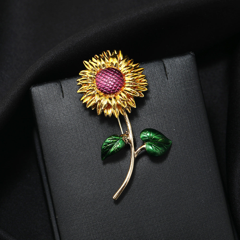 This charming brooch captures the warmth of a sunflower, with intricately detailed gold petals radiating from a rich purple center. Delicate green enamel leaves add a touch of natural vibrancy, while the slender gold stem completes the lifelike design. Perfect for adding a cheerful, nature-inspired touch to blazers, scarves, or everyday outfits, this piece blends whimsical charm with timeless elegance.