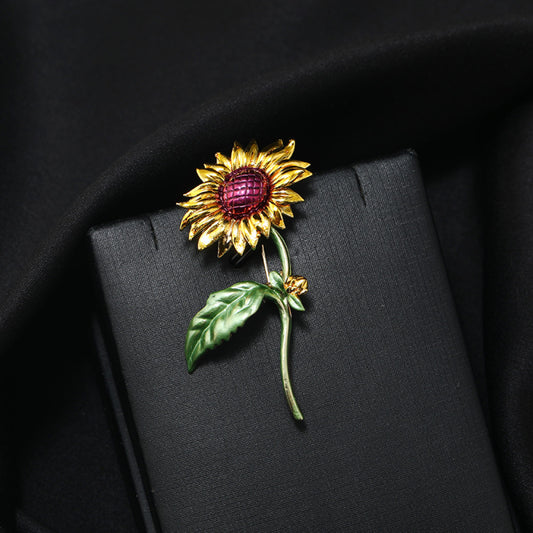 This charming brooch captures the warmth of a sunflower, with intricately detailed gold petals radiating from a rich purple center. Delicate green enamel leaves add a touch of natural vibrancy, while the slender gold stem completes the lifelike design. Perfect for adding a cheerful, nature-inspired touch to blazers, scarves, or everyday outfits, this piece blends whimsical charm with timeless elegance 01