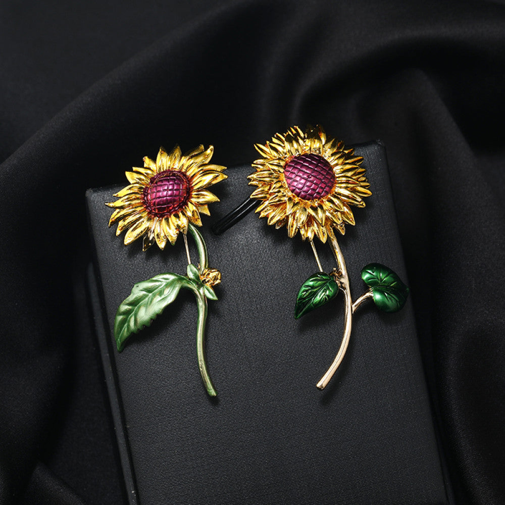 This charming brooch captures the warmth of a sunflower, with intricately detailed gold petals radiating from a rich purple center. Delicate green enamel leaves add a touch of natural vibrancy, while the slender gold stem completes the lifelike design. Perfect for adding a cheerful, nature-inspired touch to blazers, scarves, or everyday outfits, this piece blends whimsical charm with timeless elegance 02