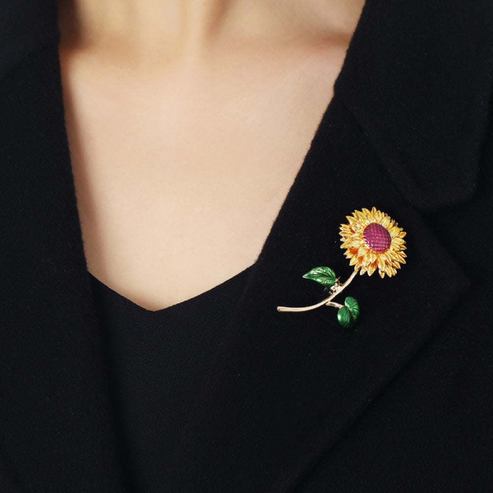 This charming brooch captures the warmth of a sunflower, with intricately detailed gold petals radiating from a rich purple center. Delicate green enamel leaves add a touch of natural vibrancy, while the slender gold stem completes the lifelike design. Perfect for adding a cheerful, nature-inspired touch to blazers, scarves, or everyday outfits, this piece blends whimsical charm with timeless elegance 03