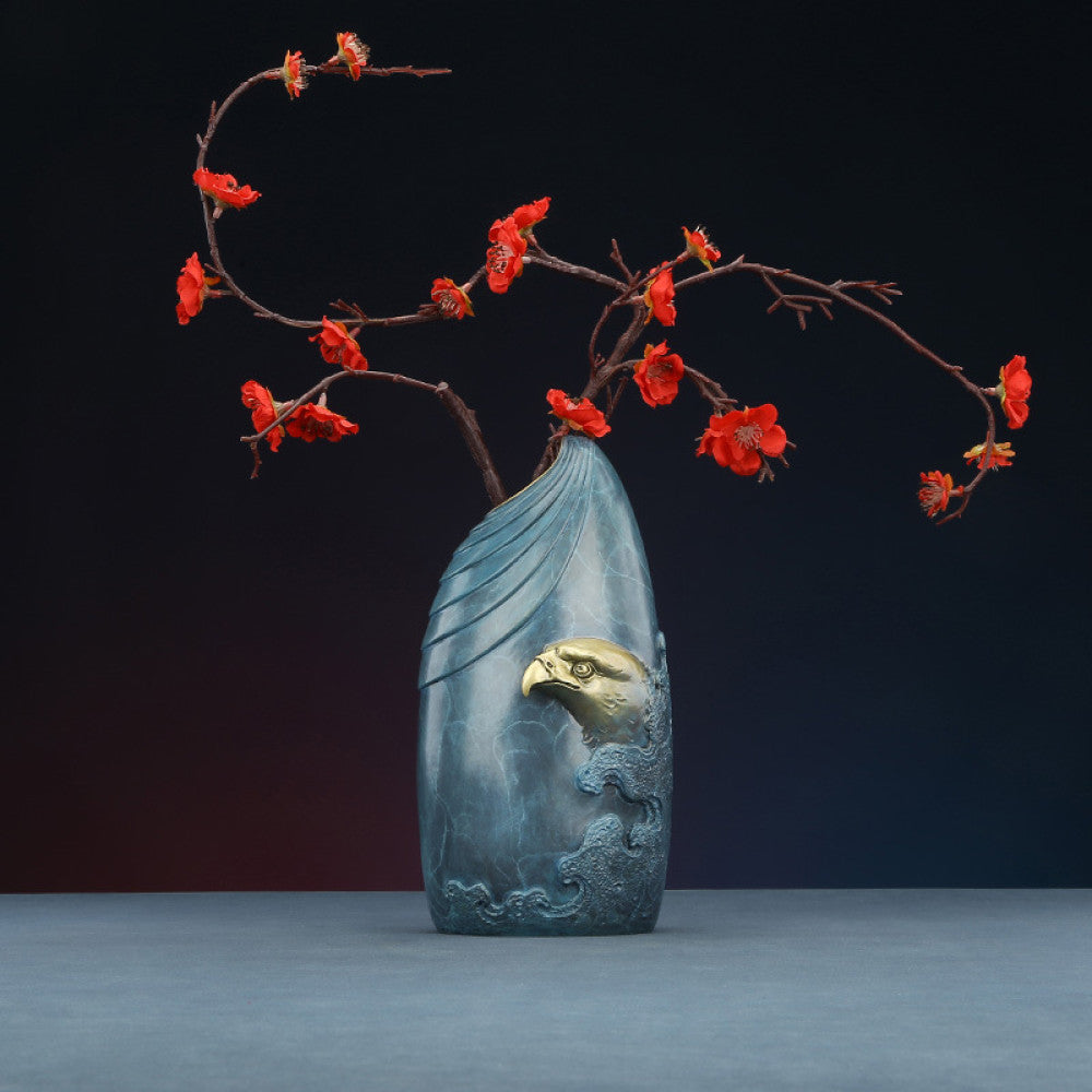 Blue textured vase with brass eagle head decoration, holding red plum blossom branches against dark gradient background