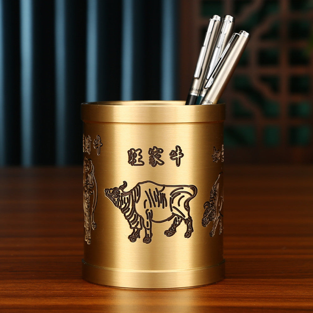 Brass pen holder with ox carving and Chinese characters, holding pens, placed on a wooden table against a traditional Chinese background