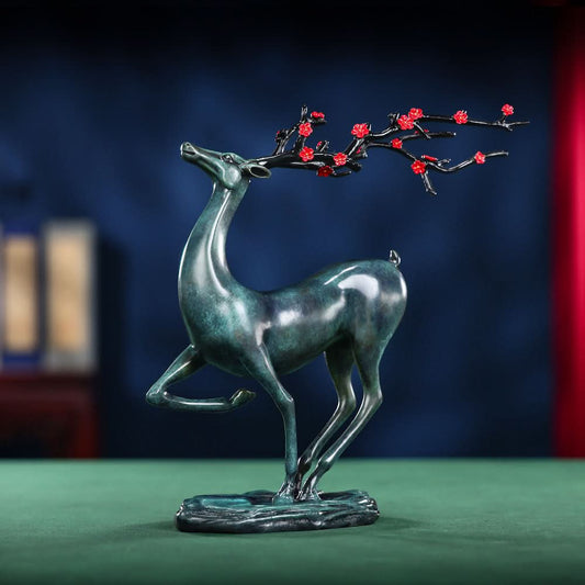 Traditional Chinese bronze deer statue with red plum blossom branch, in an elegant pose, placed on a green surface against a dark blue background 01