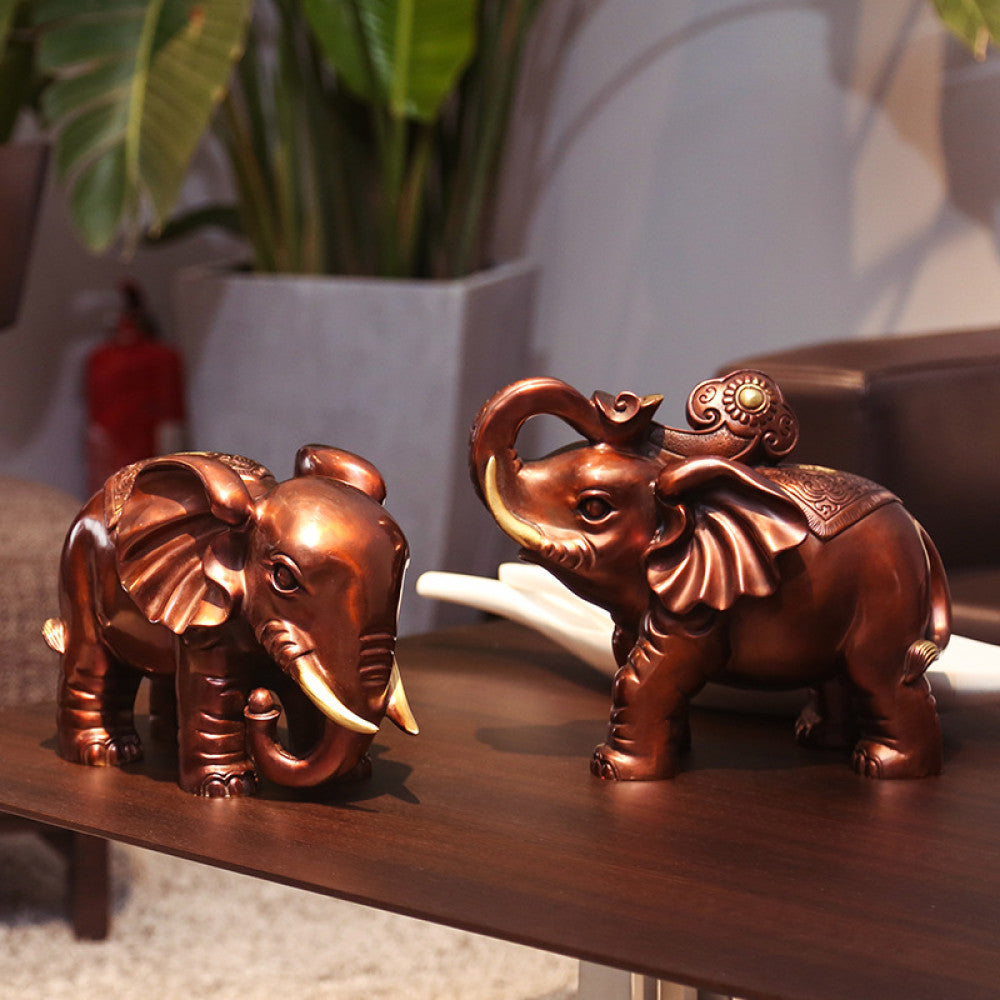 Pair of traditional Chinese bronze elephant statues with golden details, one with a curled trunk and one holding an ornament, placed on wooden bases against a dark blue background 01