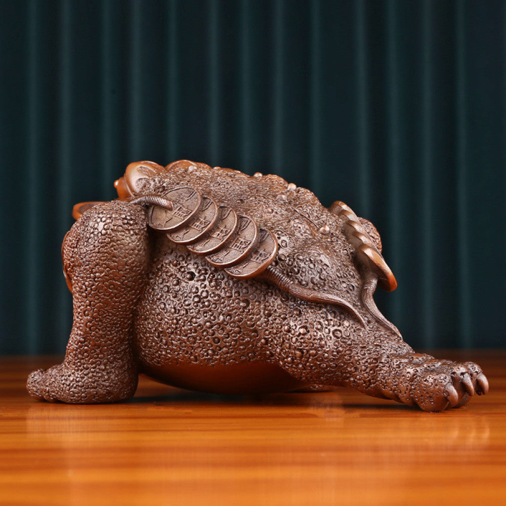 Traditional Chinese bronze money toad statue with a copper coin in its mouth, positioned on a wooden surface against a dark curtain background 01