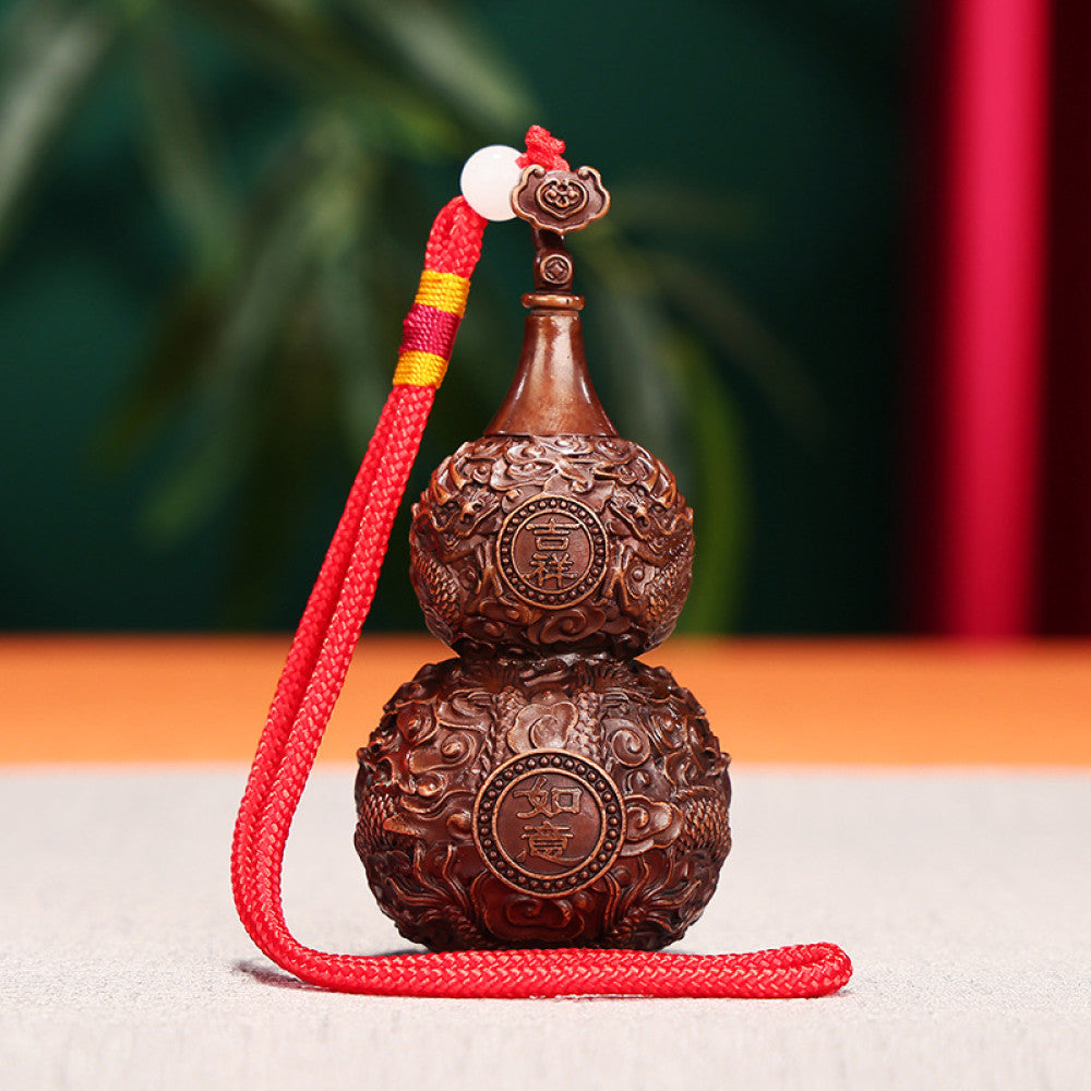 Traditional Chinese carved wooden gourd ornament with intricate patterns and red cord, placed against a blurred green plant background