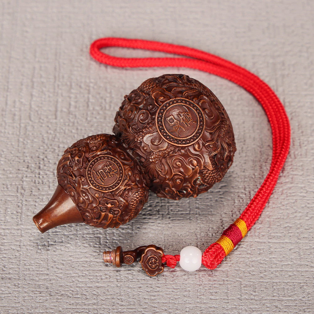 Traditional Chinese carved wooden gourd ornament with intricate patterns and red cord, placed against a blurred green plant background 03