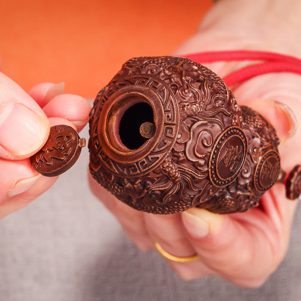 Traditional Chinese carved wooden gourd ornament with intricate patterns and red cord, placed against a blurred green plant background 06