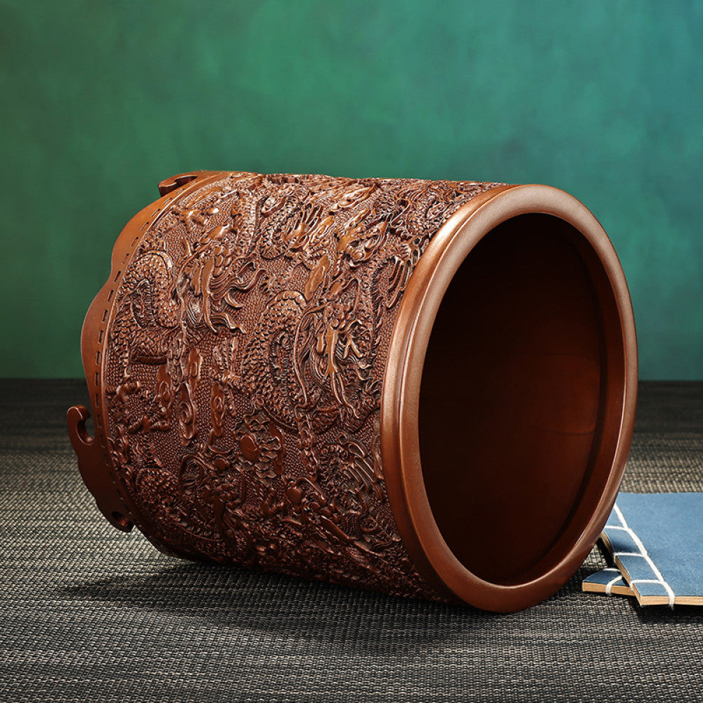 Red copper brush pot with intricate dragon and cloud carvings, placed on a textured surface against a teal background 02