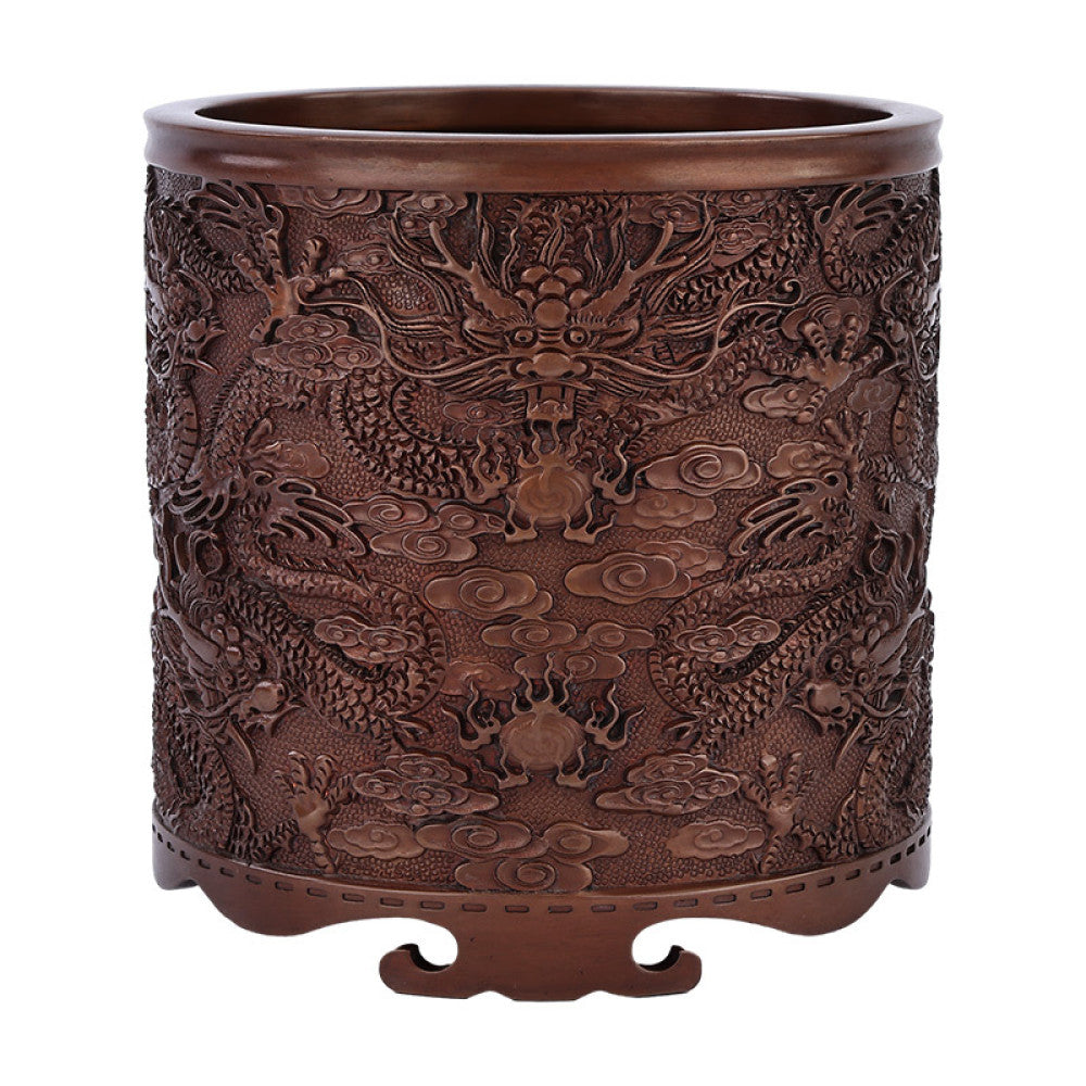 Red copper brush pot with intricate dragon and cloud carvings, placed on a textured surface against a teal background 03