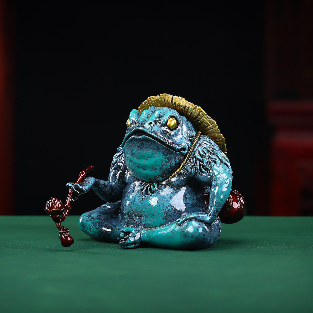 Colorful Chinese money toad statue with a straw hat, holding a ruyi - like ornament, placed on a green surface against a dark background