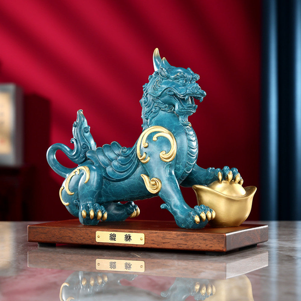 Traditional Chinese Feng Shui Pi Xiu statue in blue-green with gold inlay, holding a gold ingot, placed on a wooden base against a red background