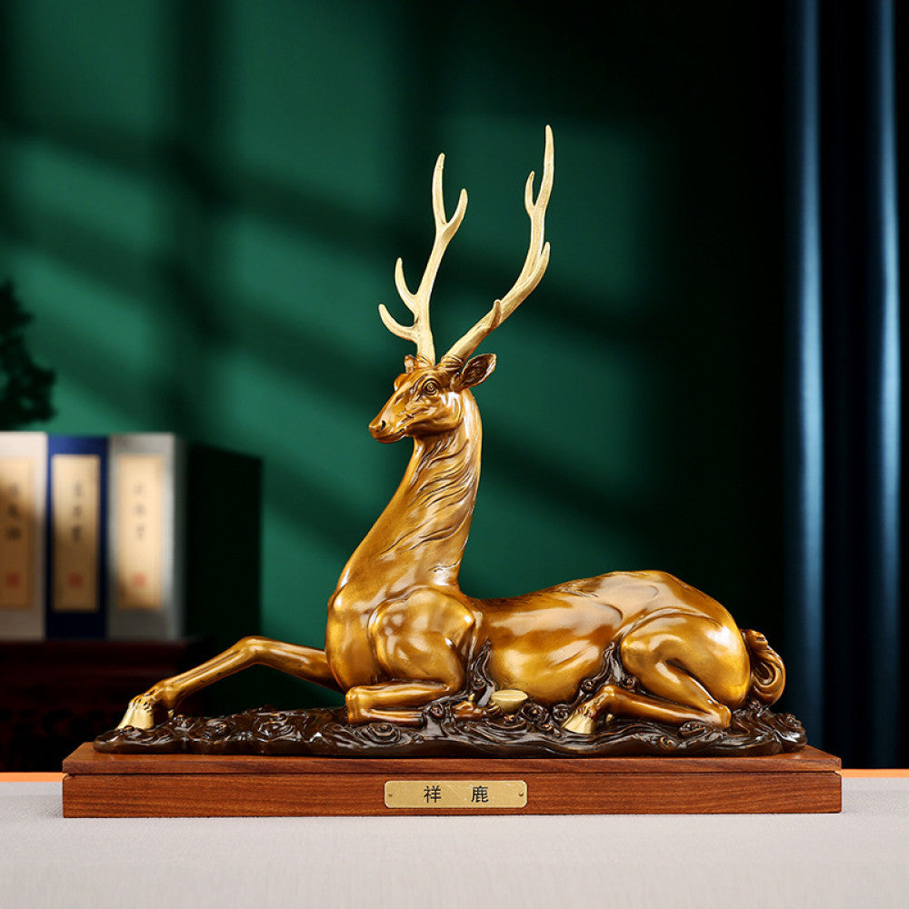 Traditional Chinese golden bronze deer statue in a reclining pose with detailed antlers, placed on a wooden base against a dark green background with traditional books