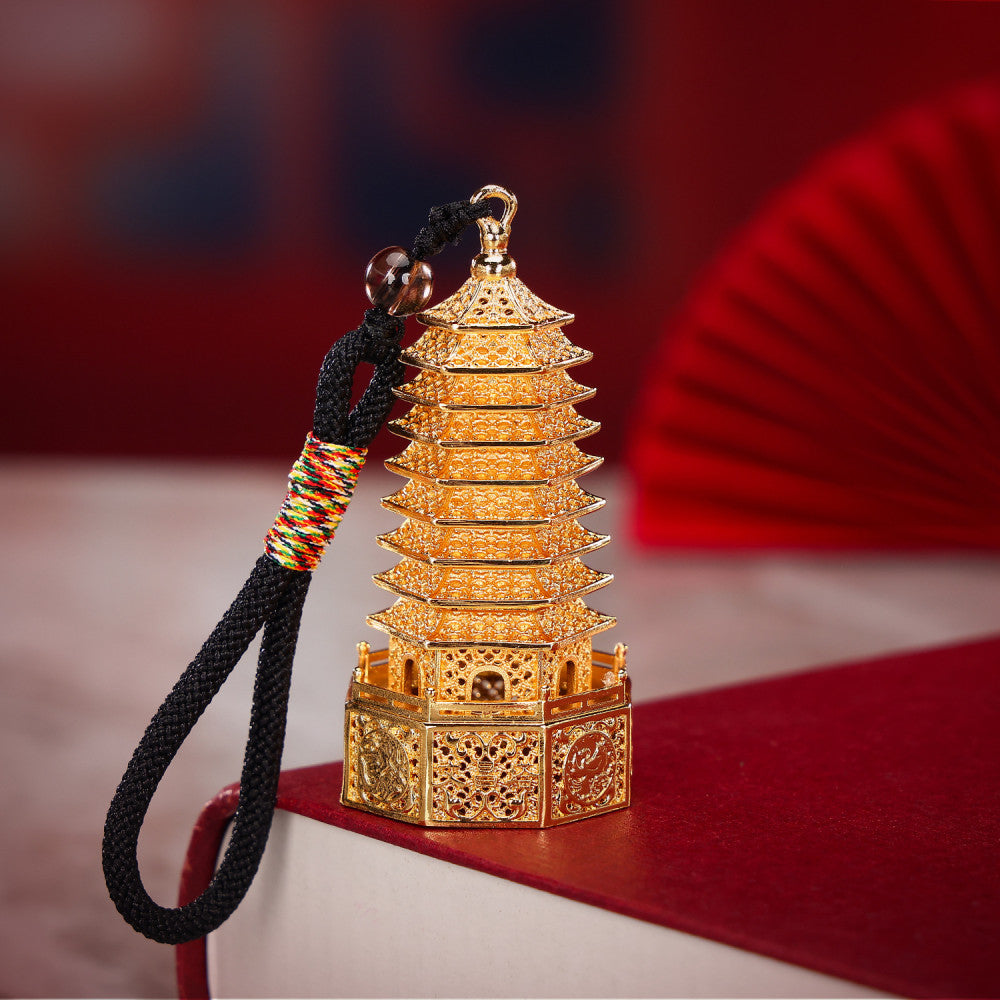 Golden Chinese Wenchang Tower pendant with intricate carvings, attached to a black cord with colorful details and beads, isolated on white background