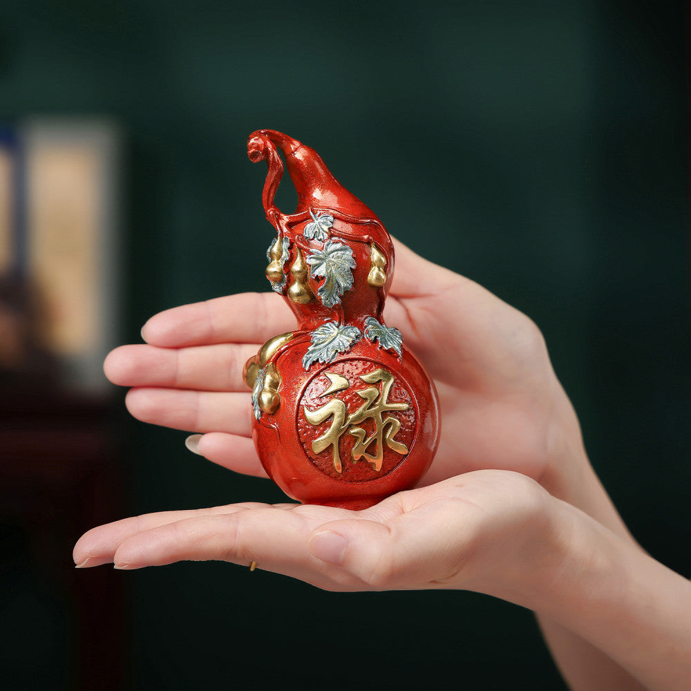 Hands holding traditional Chinese red gourd statue with "Lu" luck character and enamel details against dark background